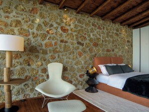 Een kamer met een stenen muur, een bed met kussens, een witte stoel en een vloerlamp.