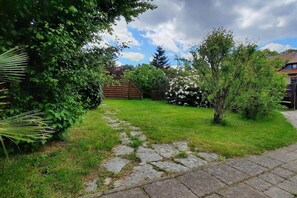 A garden with a stone pathway leading to a wooden gate, surrounded by lush greenery and flowering bushes. - Holiday home with 2 bedrooms (Plau am See)