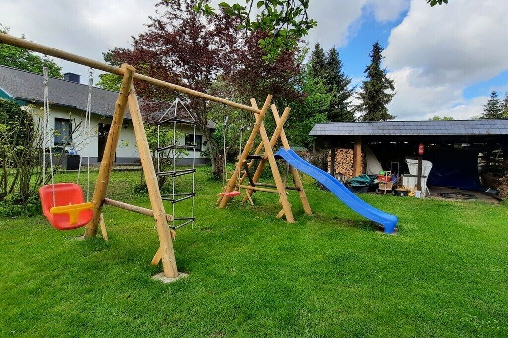 Une aire de jeux avec une balançoire, un toboggan et une petite chaise rouge et jaune.