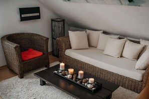 A cozy living room with a wicker sofa, a red cushion, a black coffee table with candles, and a white rug. - Holiday apartment with 2 bedrooms (Kappeln Stadt)