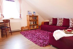 Ein gemütliches Wohnzimmer mit einer Holzhülle, einem violetten Sofa und einem Essbereich mit Stuhl und Tisch.