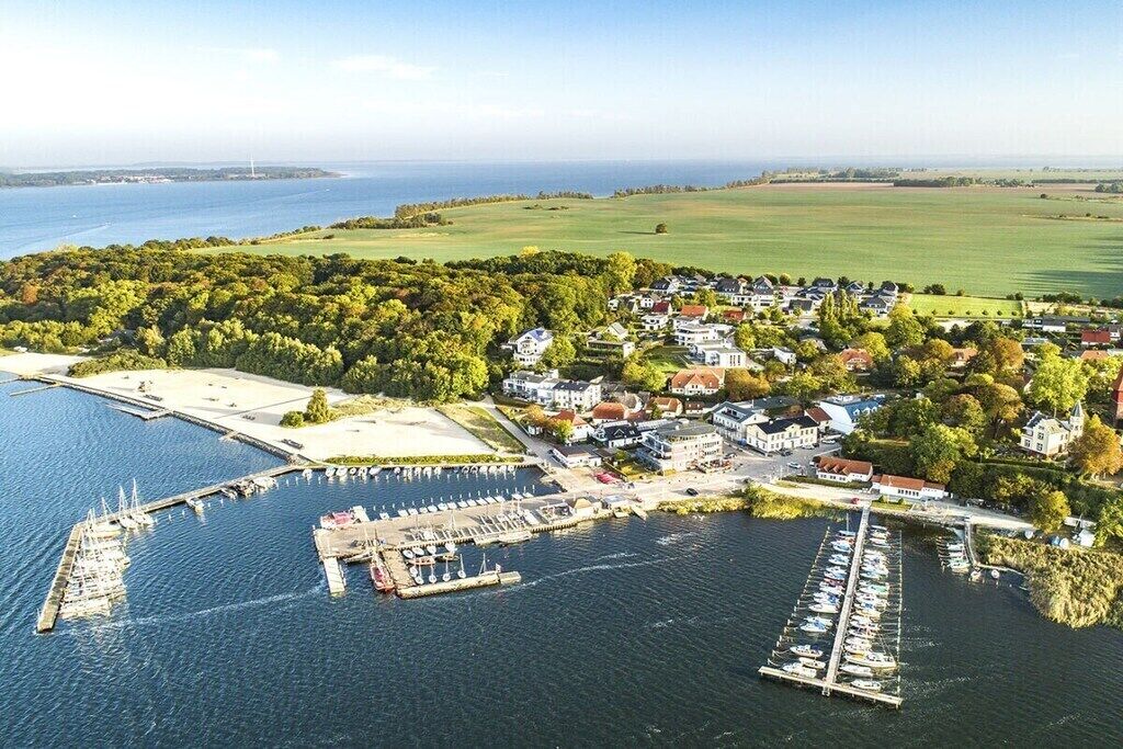 Une vue aérienne d’une ville côtière avec un port de plaisance, des immeubles résidentiels et un grand espace vert.