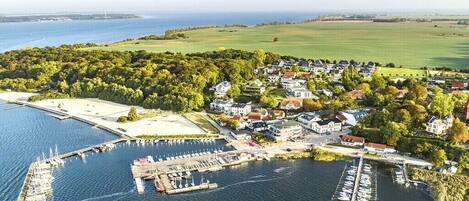 Une vue aérienne d’une ville côtière avec un port de plaisance, des immeubles résidentiels et un grand espace vert.