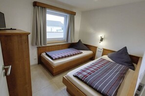 A bedroom with two beds, a wooden wardrobe, a window with curtains, and a wall-mounted light fixture. - Holiday home in Altefähr with swimming pool (Altefähr)