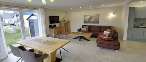 A modern living room with a dining area, a sofa, and a kitchen visible through an open door.