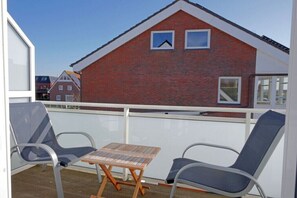 A balcony with two chairs and a small table, overlooking a red brick building with two windows. - Holiday apartment with 2 bedrooms (Norderney)