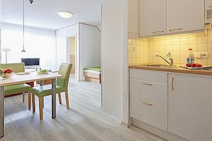 A modern kitchen with white cabinets, a wooden countertop, and a dining area with a table and chairs. - Holiday apartment with 2 bedrooms (Norderney)