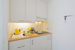 Une cuisine avec des meubles blancs, un plan de travail en bois, une bouilloire, une machine à café et une balance.