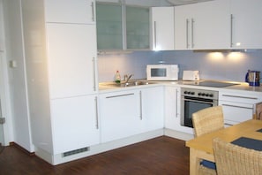 A compact kitchen with white cabinets, a microwave, a toaster, and an oven. - Captain's House Schubert (Norderney)