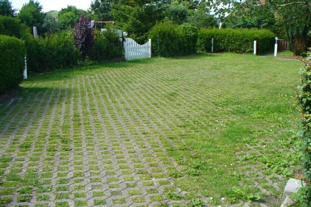 Une zone dallée, bordée d’une clôture blanche et agrémentée de verdure.