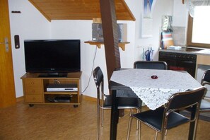 A compact living space with a television on a wooden cabinet, a dining table with chairs, and a kitchen area with a dishwasher. - Holiday apartment with 2 bedrooms (Wangerland)