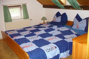 A bedroom with a bed covered in a checkered quilt, a wooden headboard, a nightstand with a lamp, and a window with curtains. - Holiday apartment with 2 bedrooms (Wangerland)