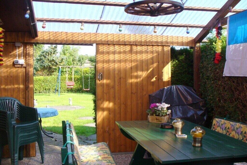 A wooden patio with a table and chairs, a covered area with a swing set, and a garden view.