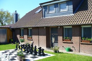 A residential building with a tiled roof, brick walls, and a checkered outdoor area with chess pieces and potted plants. - Holiday apartment with 2 bedrooms (Wangerland)