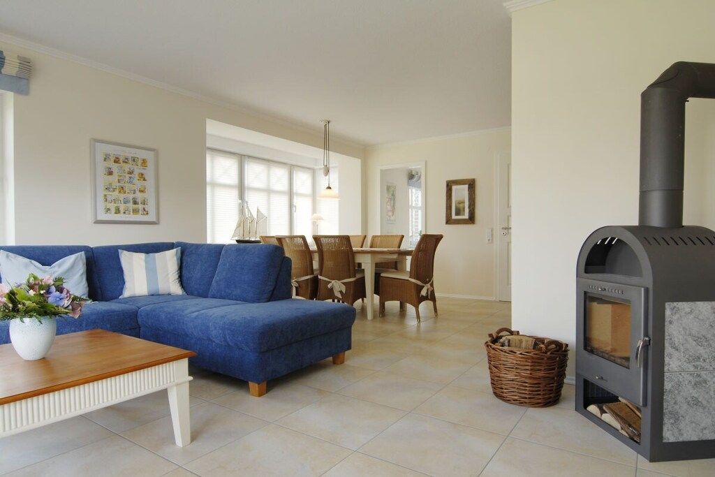 Una sala de estar con un sofá azul, una mesa de centro de madera, una chimenea y un comedor con sillas y una mesa.