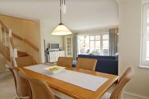 Ein Essbereich mit einem Holztisch, Korbstühlen und einer hängenden Leuchte.