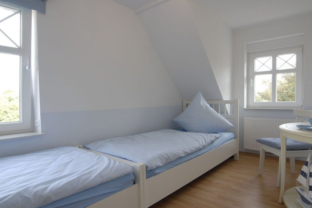 A small, single-bed room with a sloped ceiling, a window, and a small table with a chair.