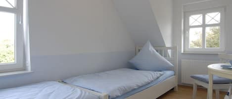 A small, single-bed room with a sloped ceiling, a window, and a small table with a chair.