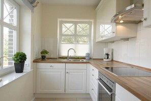 Eine moderne Küche mit weißen Schränken, einem Edelstahlbackofen, einer Spüle und einem Fenster mit Jalousien.