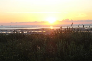 A sunset over a coastal landscape with a view of the sea and distant ships. - Holiday home with 2 bedrooms (Langenoog)