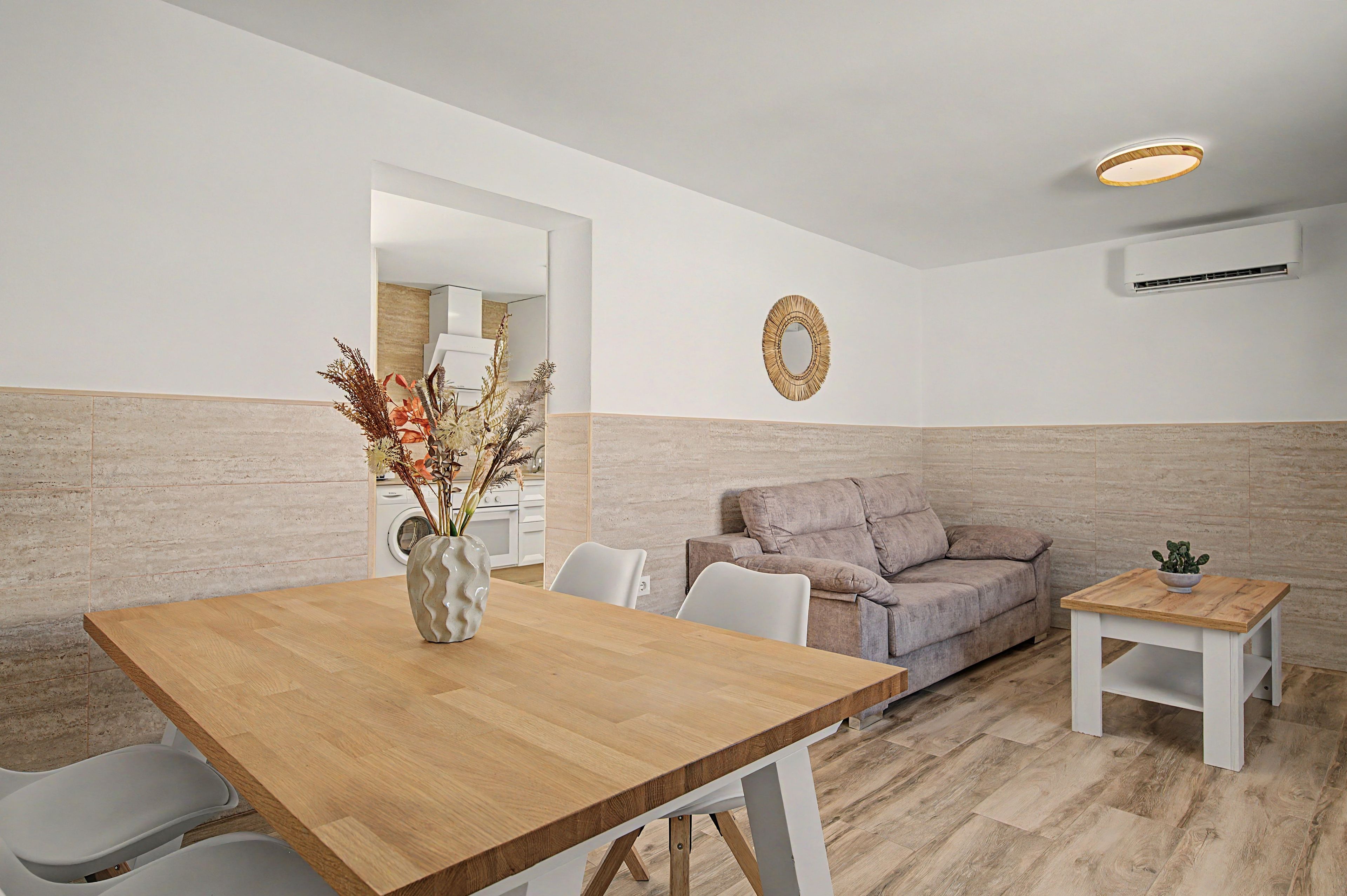 A modern living space with a wooden dining table, a grey sofa, and a small side table.