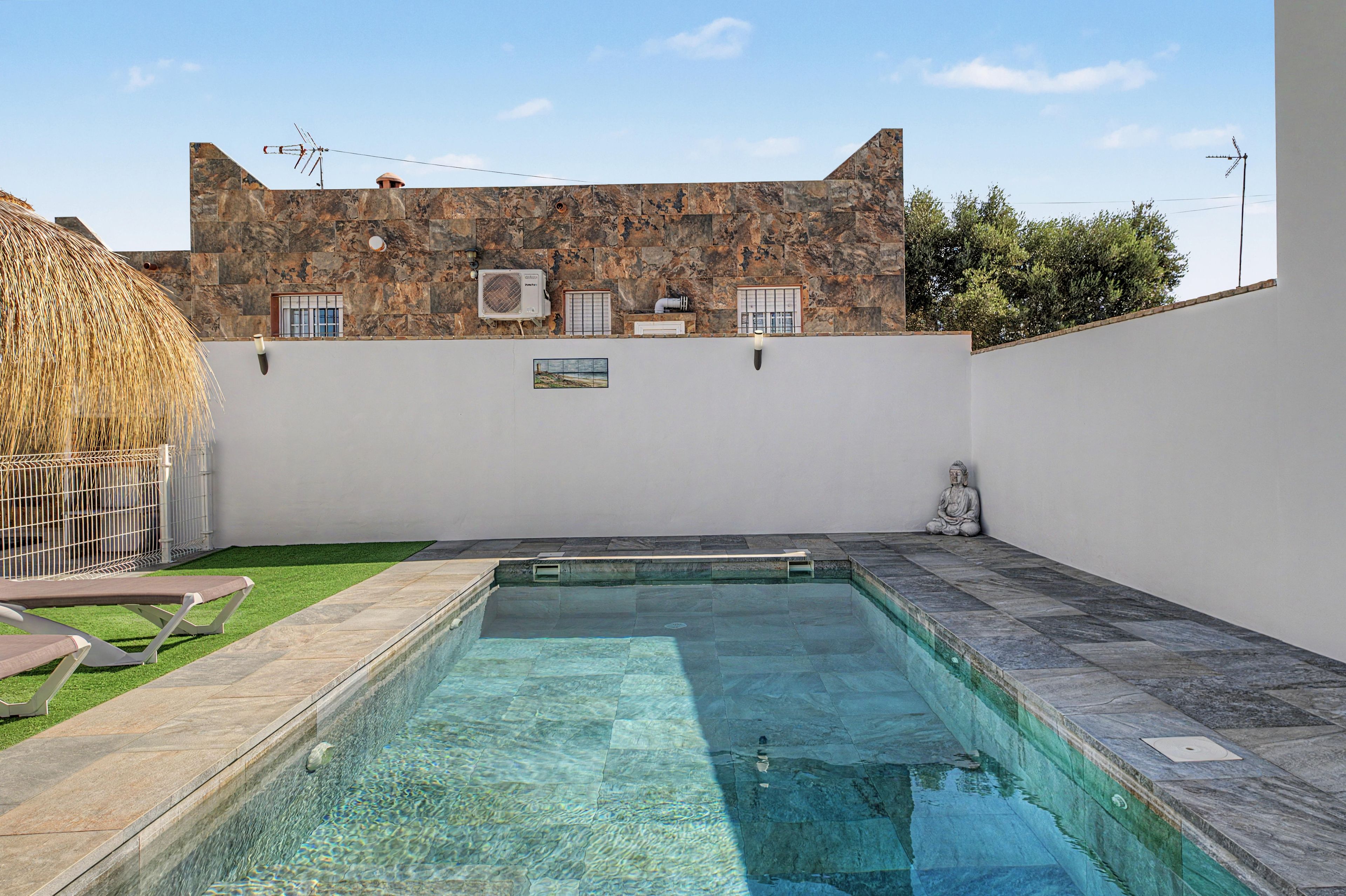 Una piscina con un muro de piedra y un edificio con ventanas y unidades de aire acondicionado.