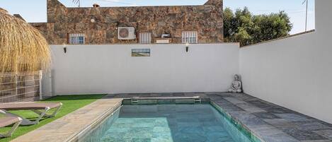 Una piscina con un muro de piedra y un edificio con ventanas y unidades de aire acondicionado.