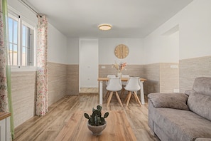 A modern living room with a wooden floor, a grey sofa, a dining table with chairs, and a cactus plant. - Holiday Home 'La Casa De Los Abuelos' with Private Pool in Conil (Conil de la Frontera)