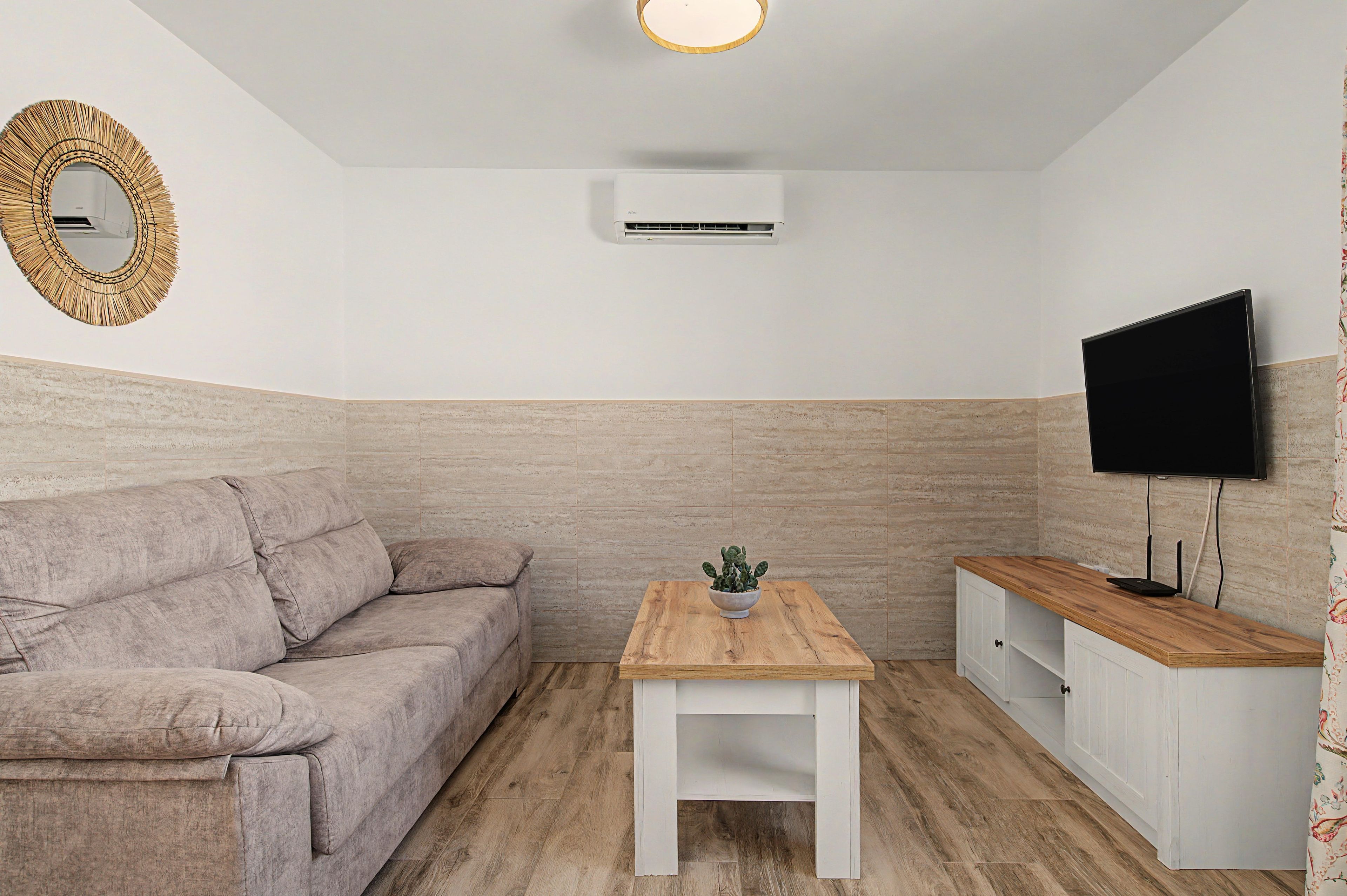 A living room with a sofa, a wooden coffee table, a television, and an air conditioning unit.