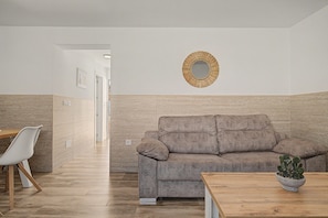A modern interior with a grey sofa, a wooden table, and a wall-mounted mirror. - Holiday Home 'La Casa De Los Abuelos' with Private Pool in Conil (Conil de la Frontera)