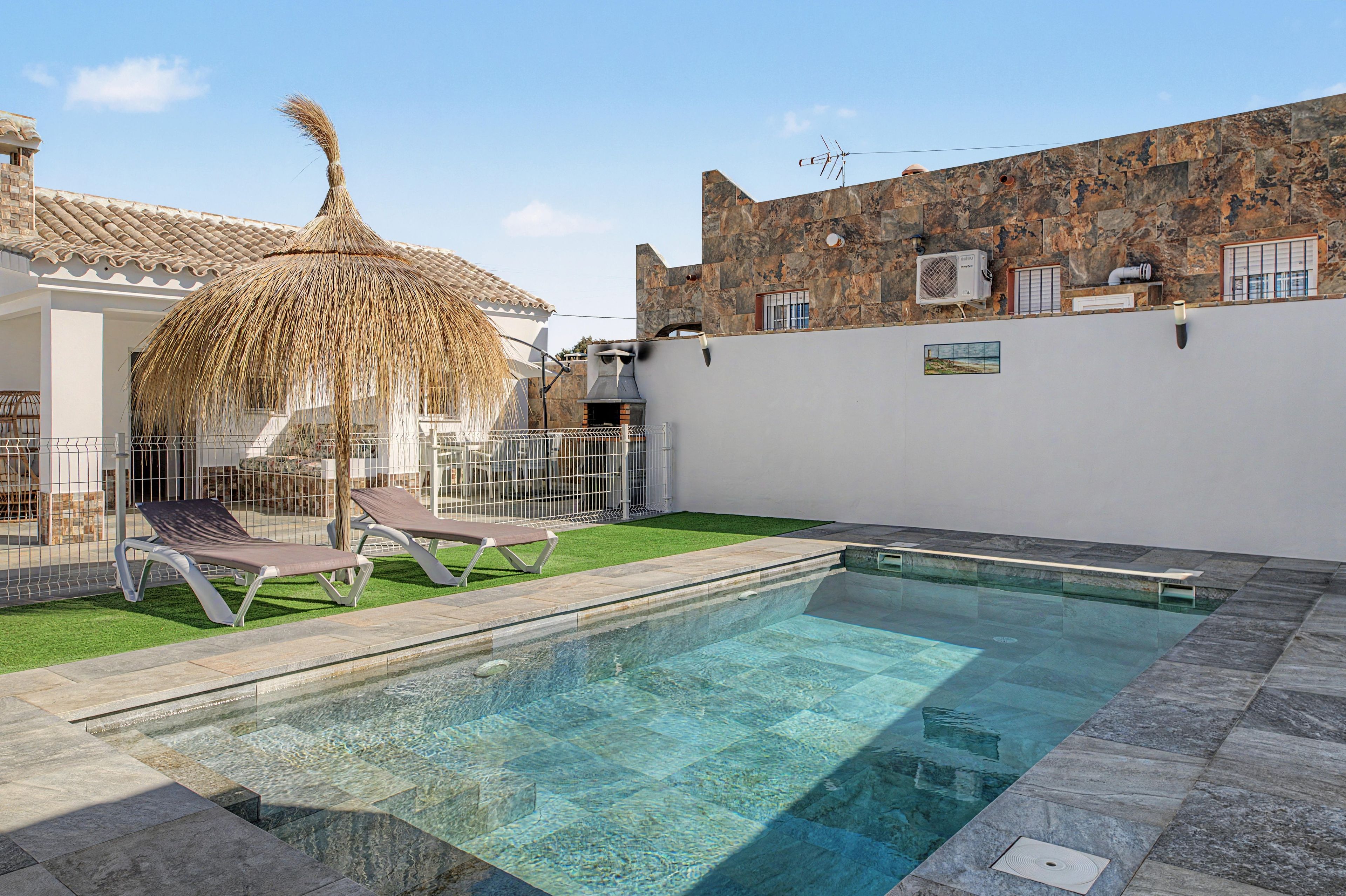 A swimming pool with clear water, surrounded by a stone deck and a grassy area with lounge chairs.