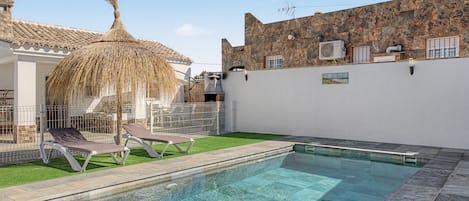 A swimming pool with clear water, surrounded by a stone deck and a grassy area with lounge chairs.