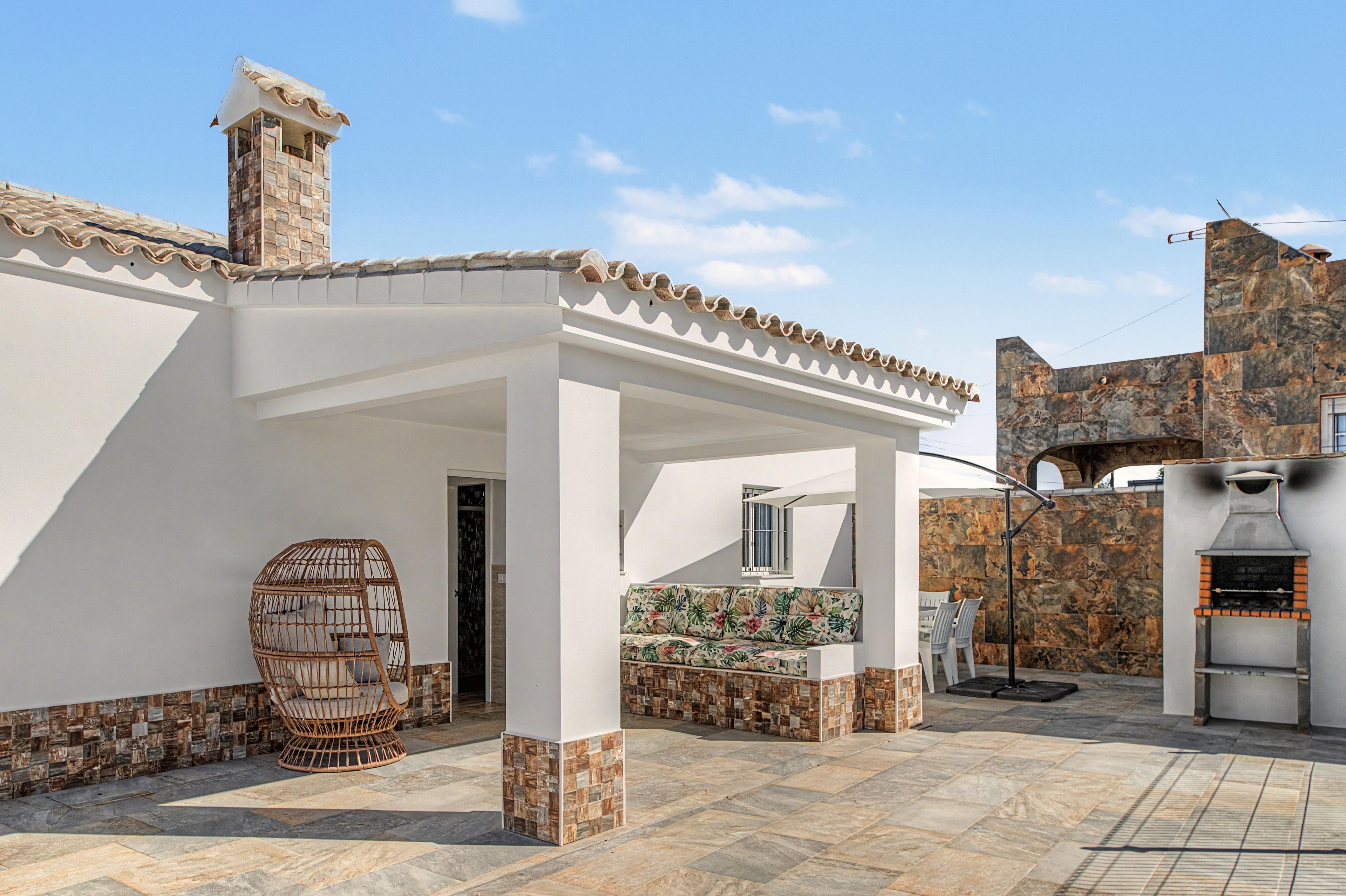 Un espacio de patio cubierto con un muro de piedra, una silla de mimbre y una parrilla.