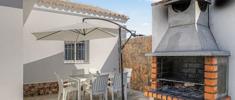 An outdoor patio with a grill, white chairs, and a table.
