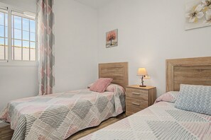 Een slaapkamer met twee bedden, een nachtkastje met een lamp, een raam met gordijnen en een muur met een ingelijste foto.