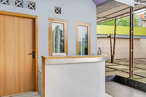 A reception desk with a wooden door and two windows, one with a view of trees and the other with a view of a building. - Luxury Deluxe DBL Retreat W/ Free Wifi and Parking (Surakarta)