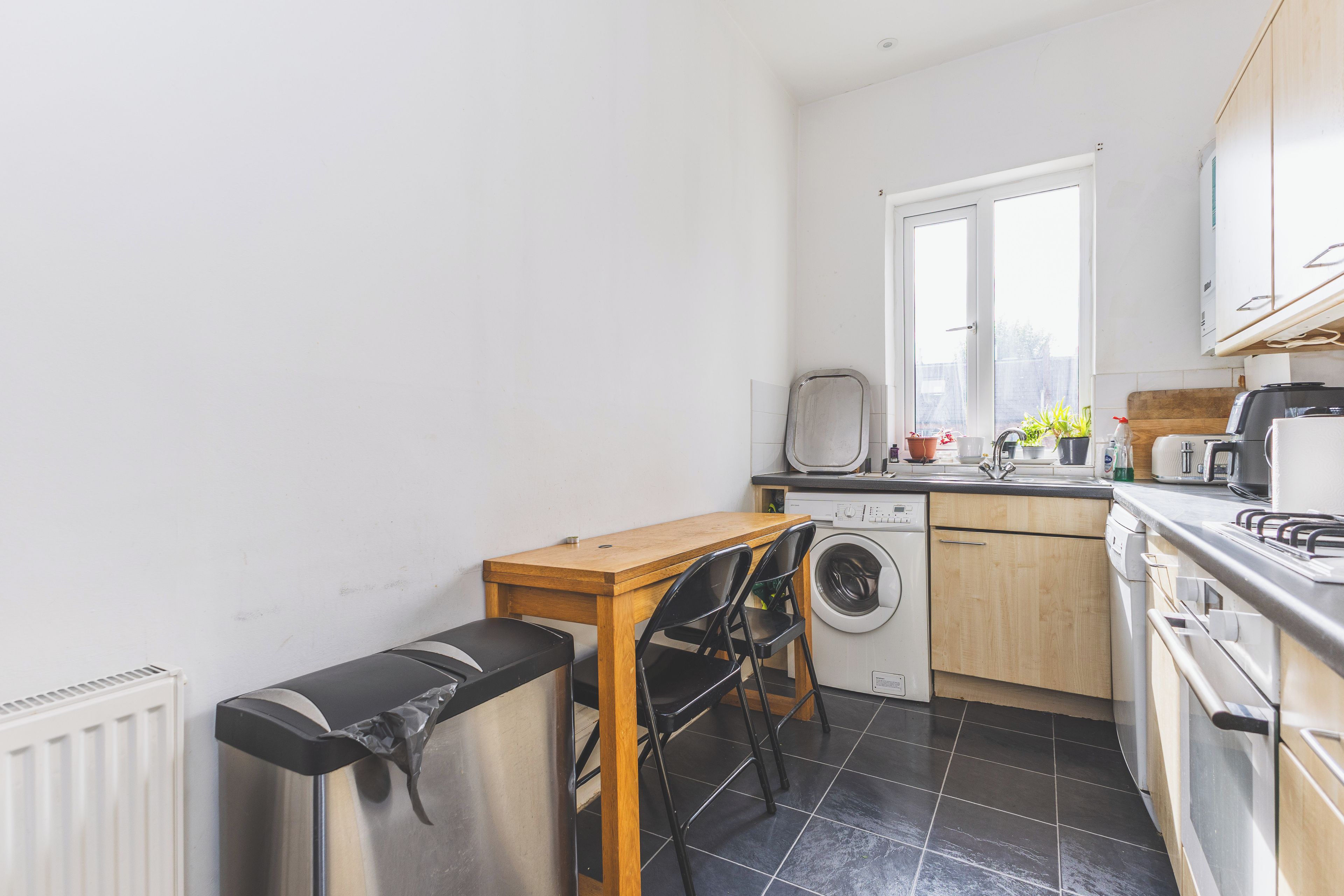 A compact kitchen with a washing machine, a table with chairs, and a radiator.
