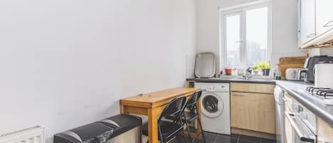 A compact kitchen with a washing machine, a table with chairs, and a radiator.