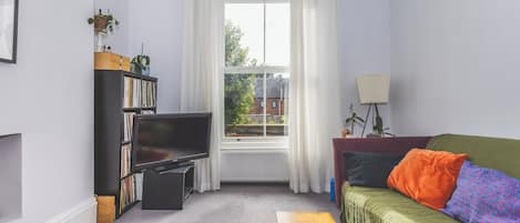 A living room with a television, bookshelf, sofa, and a window with curtains.