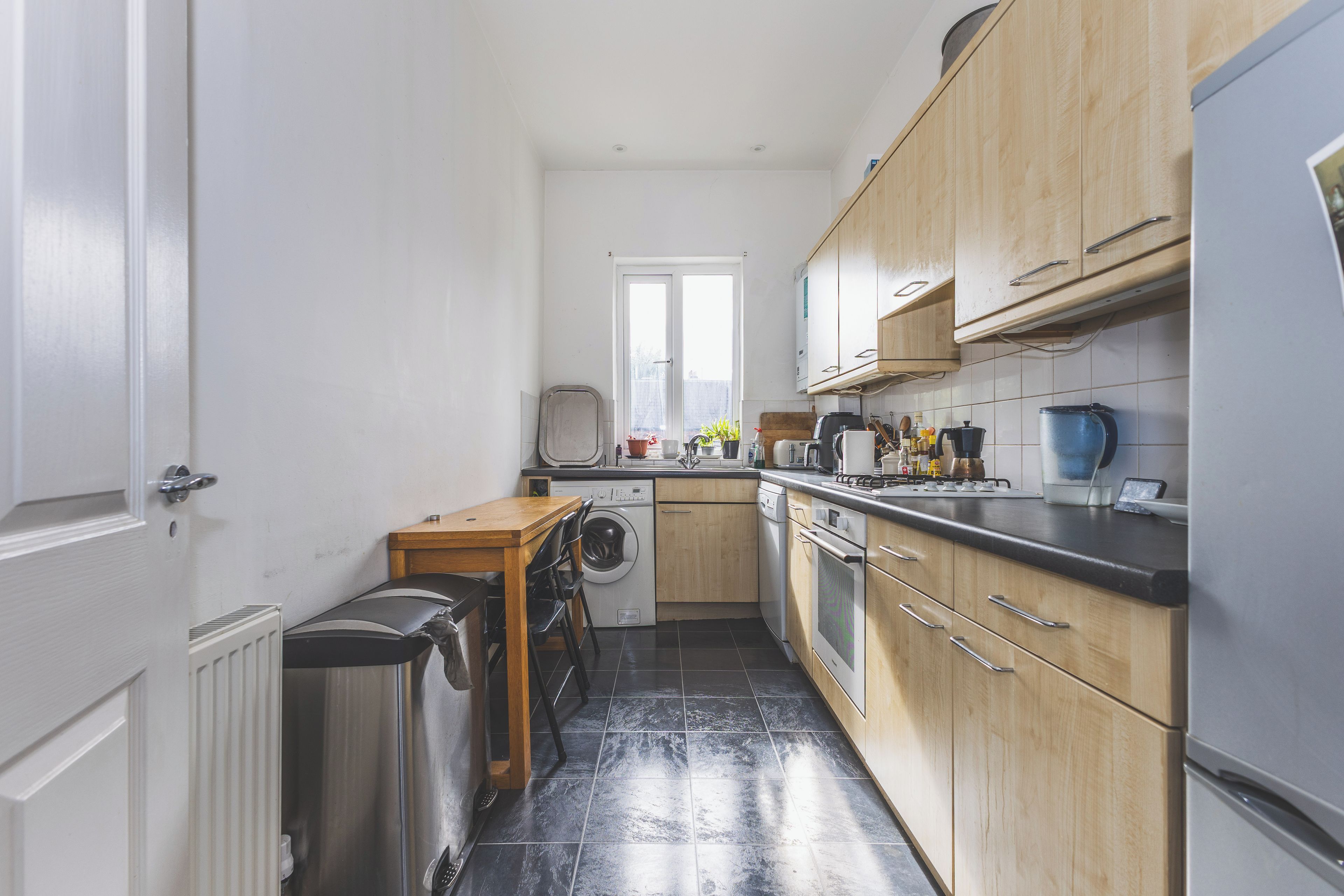 Une cuisine de taille réduite équipée d’un lave-linge, d’un évier et d’une cuisinière.
