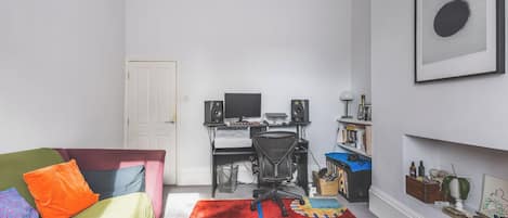 A living room with a sofa, a desk with a computer, a chair, and a bookshelf.