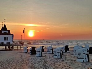 Ein Gebäude direkt am Strand mit einer Flagge, einem Steg und Strandliegen mit Preisen.