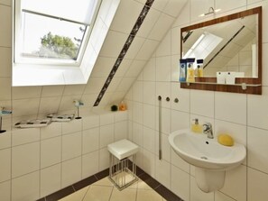 Ein Badezimmer mit Oberlicht, einem weißen Waschbecken, einem Spiegel und einem kleinen Hocker.