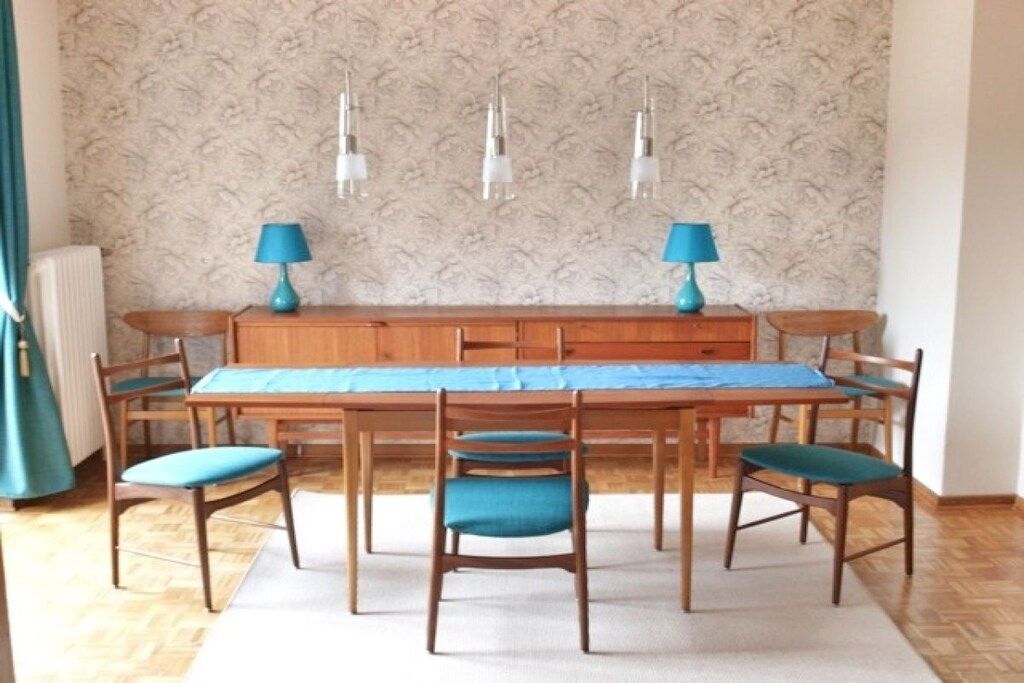 A dining area with a wooden table and chairs, a patterned wallpaper background, and pendant lights.