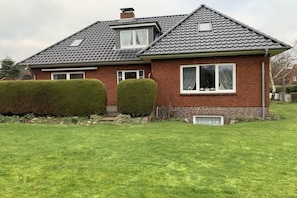 Een twee verdiepingen tellend huis met een pannendak, een klein raam met een witte omlijsting en een verzorgd gazon.