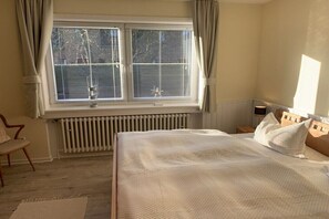 A bedroom with a large bed, a window with blinds, a radiator, a chair, and a bedside table. - Dike warden - Directly in Wyk (Wyk\/Föhr)