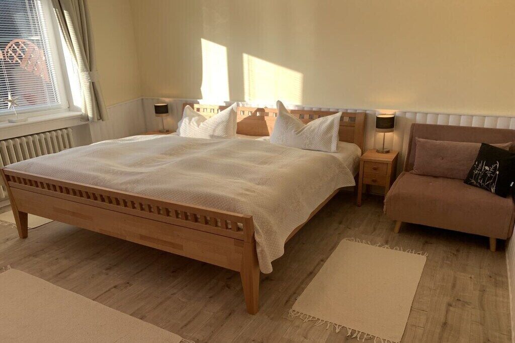 Ein Schlafzimmer mit einem hölzernen Bett, Nachttischen, einem Beistelltisch und einem Sessel.