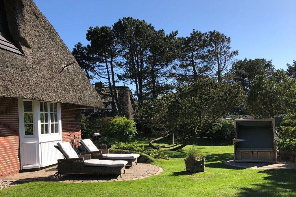 A thatched-roof building with a white door, a small garden with a lawn, and a wooden structure with a screen.