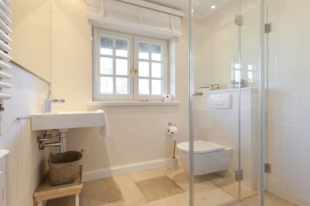 Une salle de bain avec une douche à parois de verre, un lavabo blanc et une fenêtre située au-dessus du lavabo.