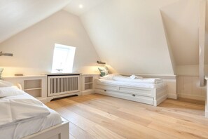 Une chambre avec un plafond en pente, un lit, un radiateur et une fenêtre.